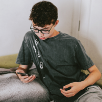 foto de un adolescente latino mirando la pantalla de su teléfono celular mientras realiza una teleconferencia
